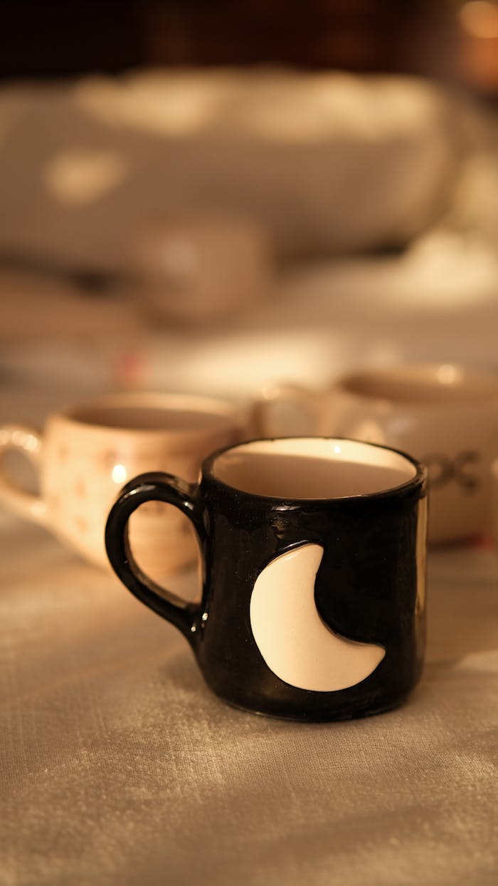 A black ceramic coffee mug featuring a moon design, highlighted in warm lighting, perfect for cozy mornings.